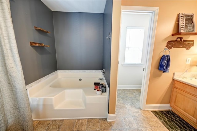 bathroom with vanity, a bath, and baseboards