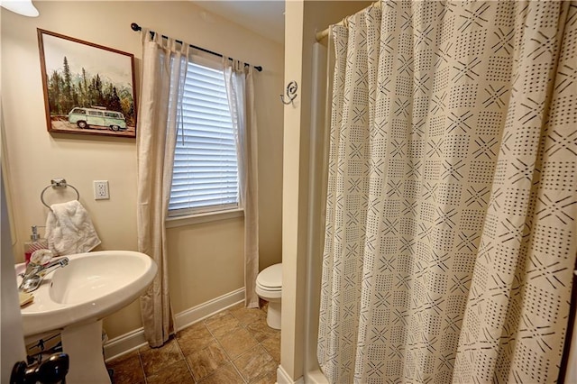 bathroom with toilet, stone finish floor, baseboards, and a shower with shower curtain