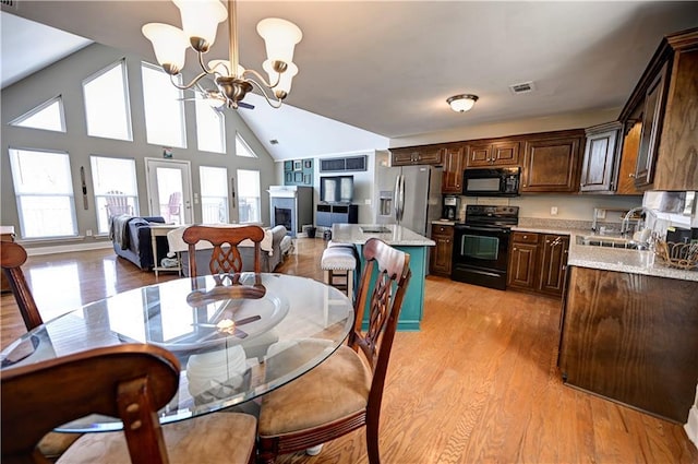 dining space featuring high vaulted ceiling, a fireplace, visible vents, light wood-type flooring, and an inviting chandelier