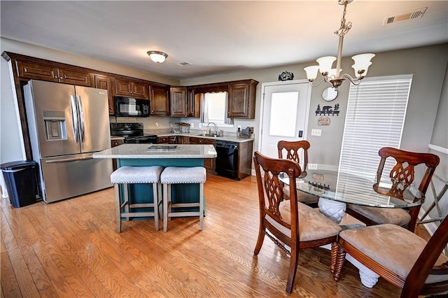 kitchen featuring light wood-style flooring, dark brown cabinetry, a sink, visible vents, and black appliances