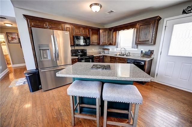 kitchen featuring a sink, visible vents, light wood-style floors, black appliances, and a kitchen bar