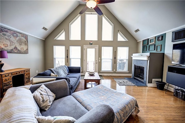 living area featuring high vaulted ceiling, a fireplace with flush hearth, visible vents, and wood finished floors