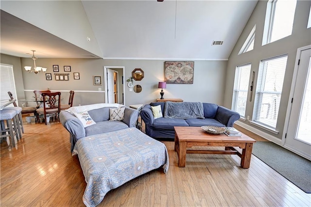 living area with high vaulted ceiling, light wood-type flooring, visible vents, and an inviting chandelier