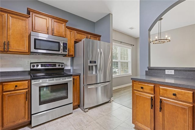 kitchen featuring light tile patterned flooring, appliances with stainless steel finishes, tasteful backsplash, hanging light fixtures, and a notable chandelier