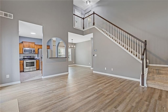 unfurnished living room featuring a towering ceiling, an inviting chandelier, and light wood-type flooring