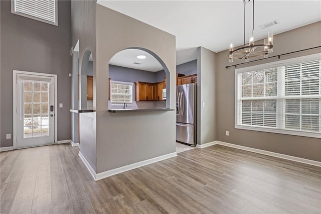 kitchen with hanging light fixtures, a wealth of natural light, stainless steel fridge, and light wood-type flooring