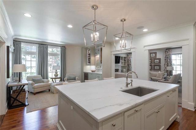 kitchen featuring sink, light stone counters, pendant lighting, a kitchen island with sink, and white cabinets