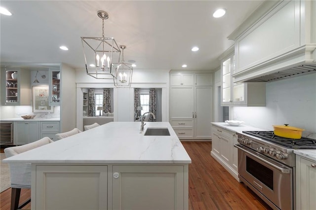 kitchen featuring pendant lighting, a center island with sink, sink, high end stainless steel range oven, and white cabinetry