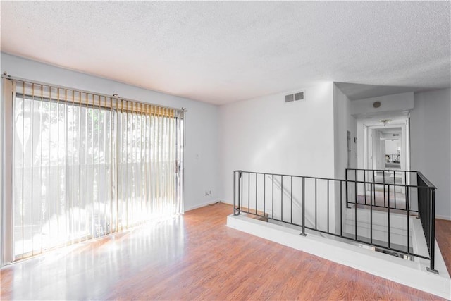 spare room featuring a textured ceiling, wood finished floors, visible vents, and baseboards