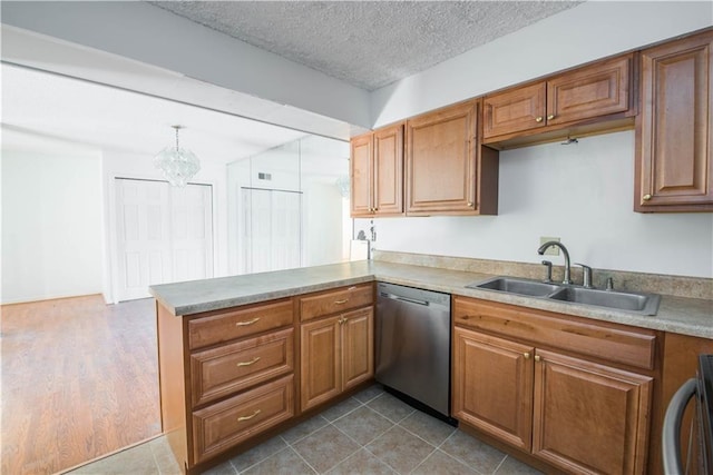 kitchen with a peninsula, stainless steel dishwasher, brown cabinetry, and a sink