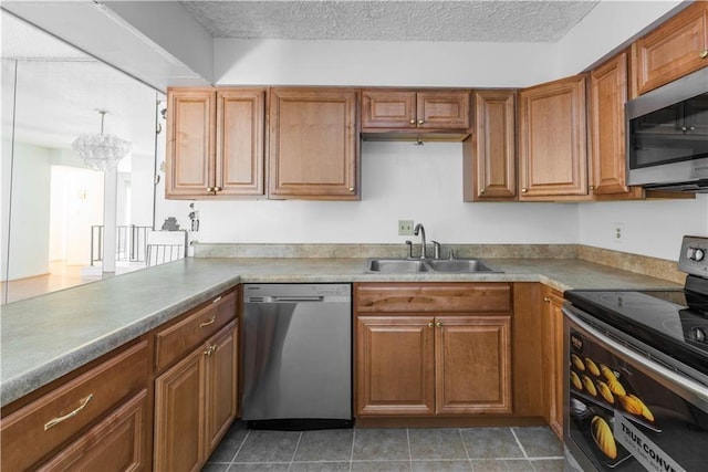 kitchen with brown cabinetry, appliances with stainless steel finishes, a textured ceiling, a sink, and light tile patterned flooring