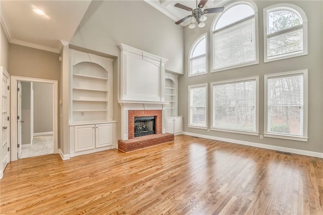 unfurnished living room with crown molding, a brick fireplace, built in shelves, and a wealth of natural light