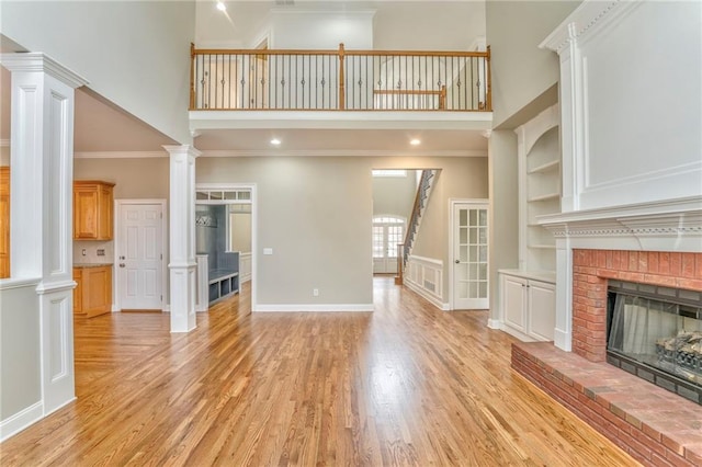 unfurnished living room with crown molding, built in features, decorative columns, a brick fireplace, and light wood-type flooring