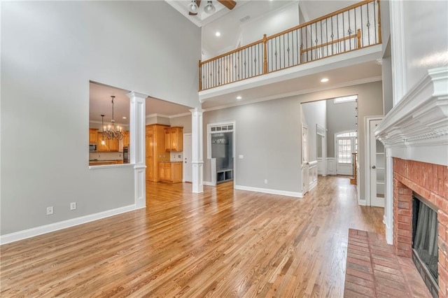 unfurnished living room with a fireplace, decorative columns, a high ceiling, ornamental molding, and light wood-type flooring