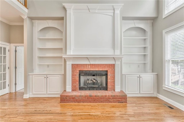 unfurnished living room with crown molding, a brick fireplace, light wood-type flooring, and built in shelves