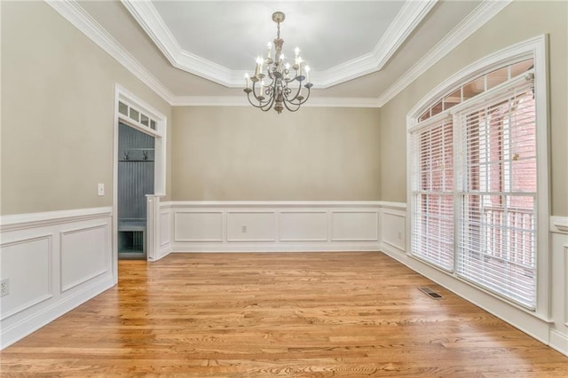 spare room with an inviting chandelier, ornamental molding, a tray ceiling, and light wood-type flooring