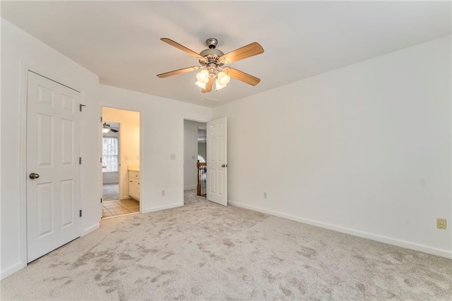 unfurnished bedroom featuring ensuite bath, light colored carpet, and ceiling fan