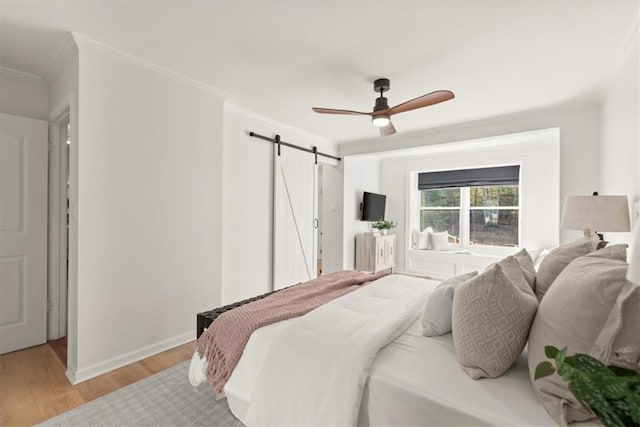 bedroom with ceiling fan, ornamental molding, a barn door, and light hardwood / wood-style flooring