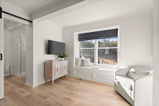 living area featuring light hardwood / wood-style floors, ornamental molding, and a barn door