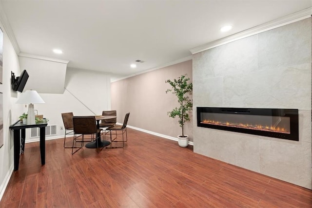 dining area featuring hardwood / wood-style flooring, crown molding, and a tiled fireplace