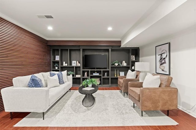 living room with built in shelves, crown molding, and hardwood / wood-style flooring