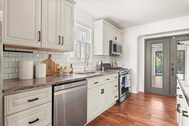 kitchen with appliances with stainless steel finishes, white cabinetry, dark stone counters, tasteful backsplash, and sink