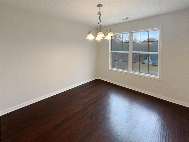 spare room featuring an inviting chandelier and dark wood-type flooring