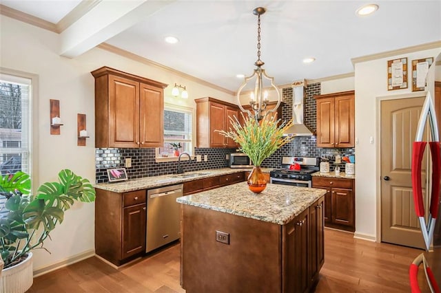 kitchen featuring wood finished floors, a sink, appliances with stainless steel finishes, wall chimney exhaust hood, and a notable chandelier