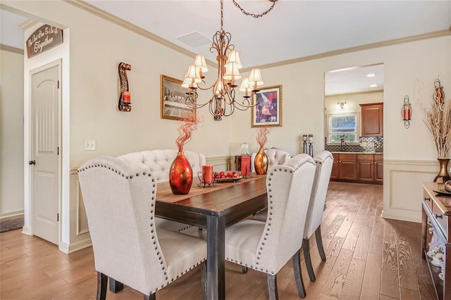 dining space with crown molding, light wood-type flooring, and an inviting chandelier