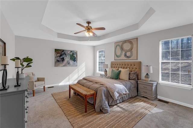 bedroom featuring baseboards, a raised ceiling, light colored carpet, and a ceiling fan