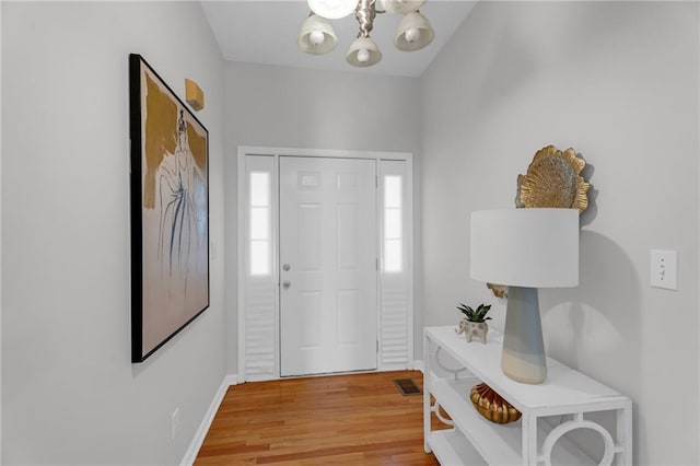 foyer entrance with visible vents, an inviting chandelier, baseboards, and light wood-style floors