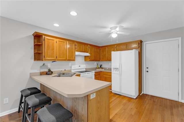 kitchen with a sink, under cabinet range hood, white appliances, a peninsula, and light countertops