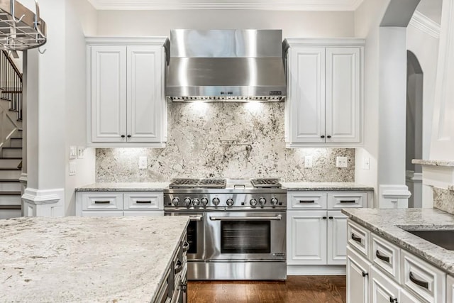 47 Fern Leaf Way, Newnan, GA 30265 - kitchen featuring wall chimney range hood, high end stainless steel range oven, arched walkways, white cabinets, and ornamental molding