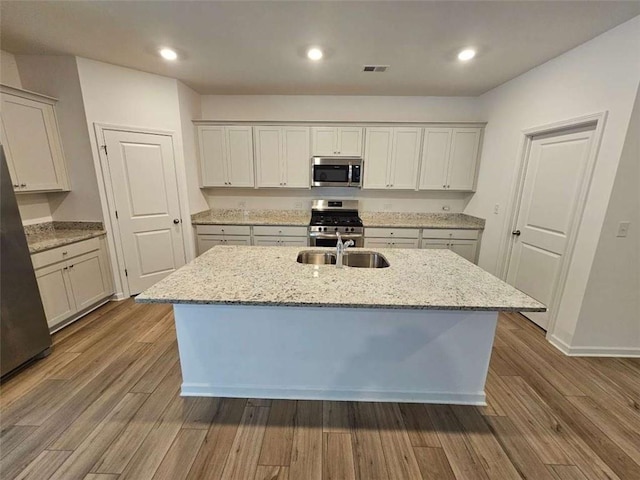 kitchen featuring light stone countertops, an island with sink, wood-type flooring, and appliances with stainless steel finishes