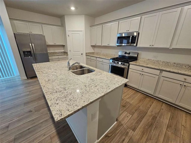 kitchen featuring sink, dark wood-type flooring, light stone counters, a kitchen island with sink, and appliances with stainless steel finishes