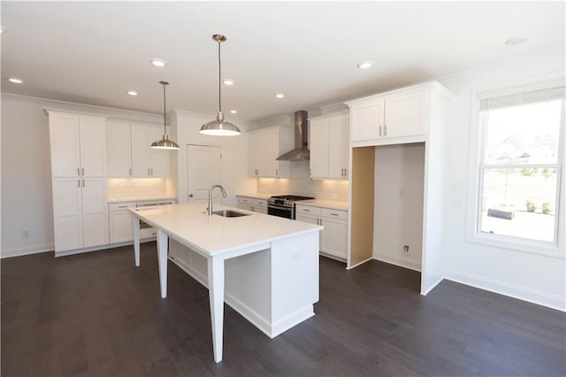 kitchen with pendant lighting, wall chimney range hood, sink, gas stove, and an island with sink