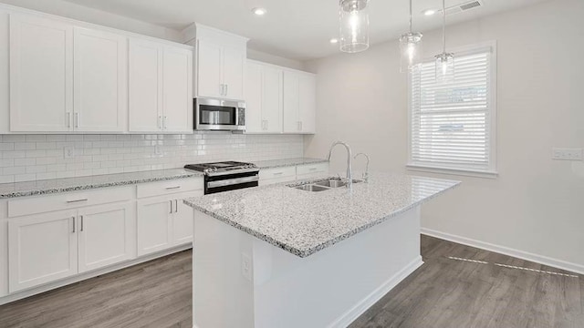 kitchen with sink, hanging light fixtures, stainless steel appliances, an island with sink, and white cabinets