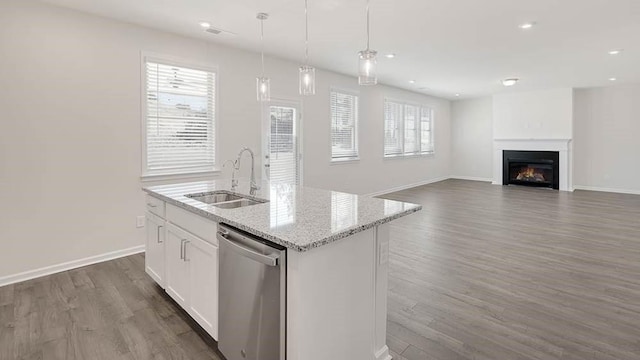 kitchen featuring sink, stainless steel dishwasher, an island with sink, a large fireplace, and white cabinetry