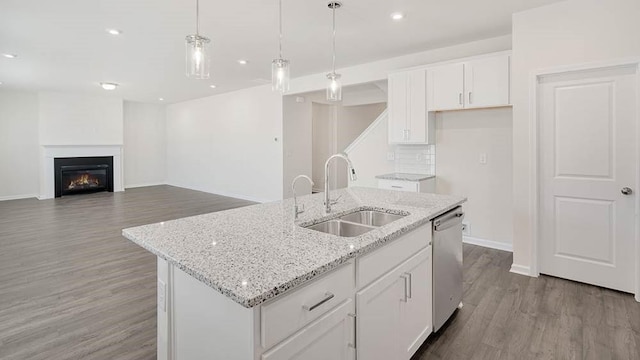 kitchen featuring stainless steel dishwasher, a kitchen island with sink, sink, pendant lighting, and white cabinets