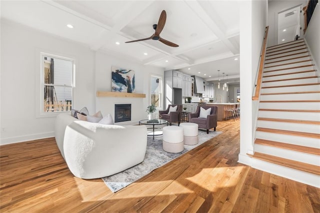 living room featuring coffered ceiling, ceiling fan, beamed ceiling, and light hardwood / wood-style flooring