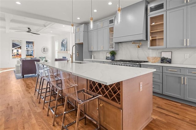 kitchen with coffered ceiling, hanging light fixtures, custom exhaust hood, and an island with sink