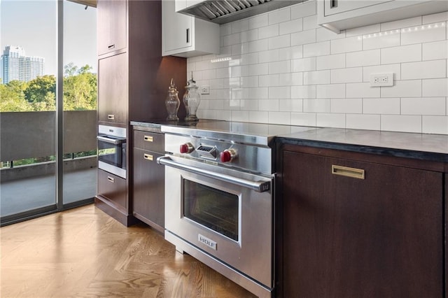 kitchen featuring decorative backsplash, light parquet floors, dark brown cabinetry, stainless steel appliances, and custom range hood