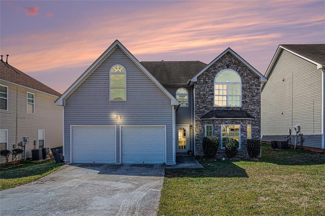 traditional-style house featuring driveway, central AC unit, stone siding, an attached garage, and a yard