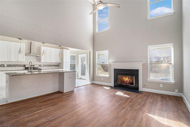 kitchen with dark wood finished floors, backsplash, a fireplace with flush hearth, white cabinetry, and wall chimney range hood