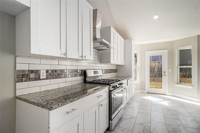 kitchen featuring marble finish floor, backsplash, wall chimney range hood, stainless steel gas range, and dark stone counters