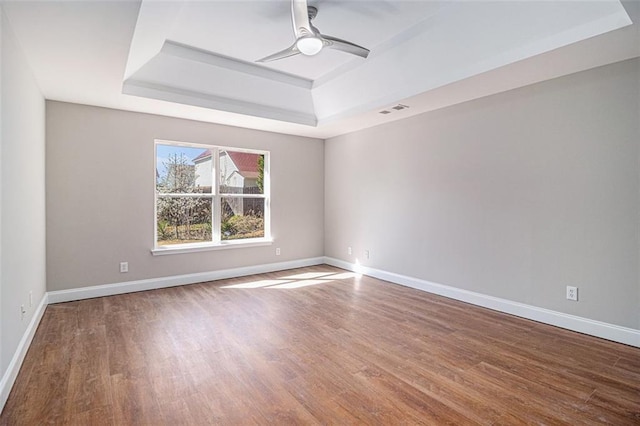 empty room with a raised ceiling, visible vents, baseboards, and wood finished floors