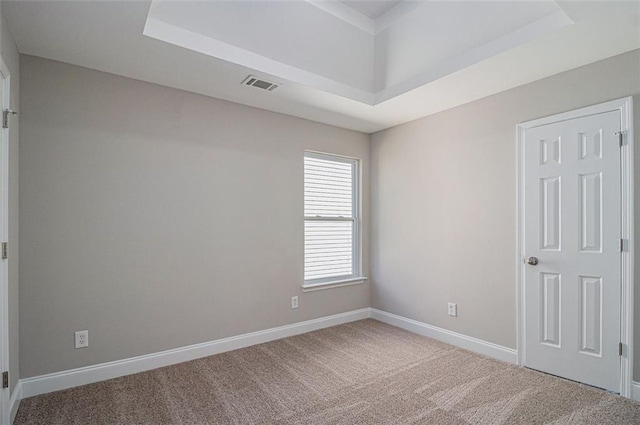 carpeted empty room with a tray ceiling, visible vents, and baseboards