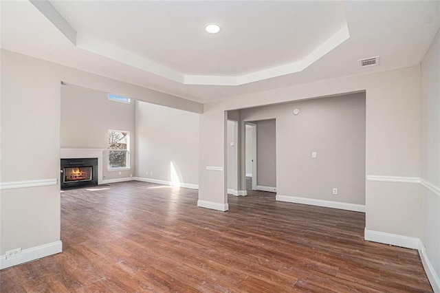 unfurnished living room with a raised ceiling, visible vents, a fireplace with flush hearth, wood finished floors, and baseboards