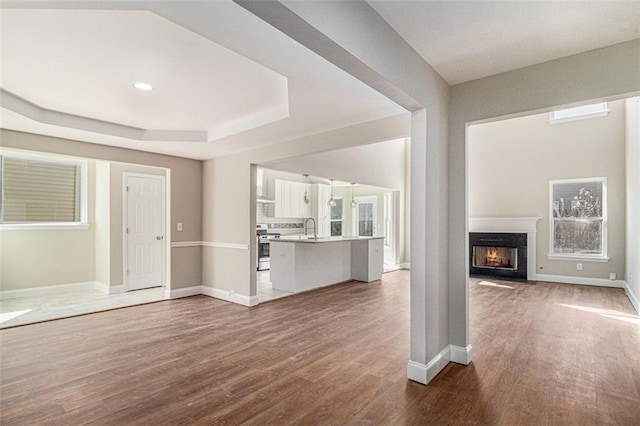 unfurnished living room with a warm lit fireplace, a sink, wood finished floors, baseboards, and a raised ceiling