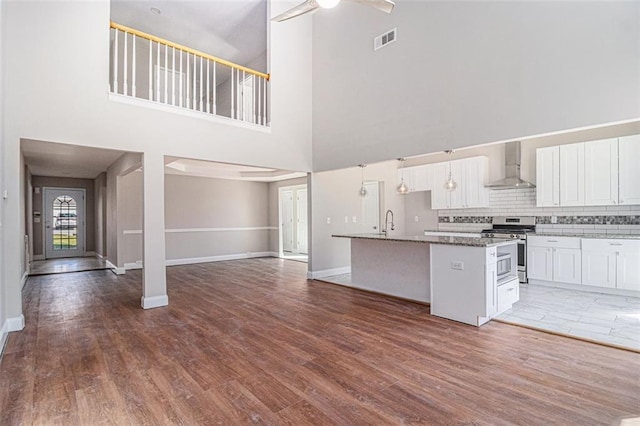 kitchen with visible vents, open floor plan, stainless steel gas stove, wall chimney range hood, and wood finished floors